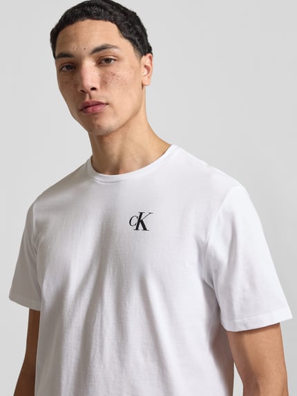 Männermodel trägt Regular Fit T-Shirt mit Logo-Print von Calvin Klein Jeans in Weiß aus reiner Baumwolle, Nahaufnahme Oberkörper.
