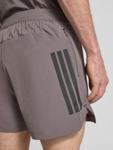 Mannenmodel draagt Regular Fit Sport-Shorts met elastische band van adidas Training, look: effen, mesh-inzet, labelprint, steekzakken. Detailopname.