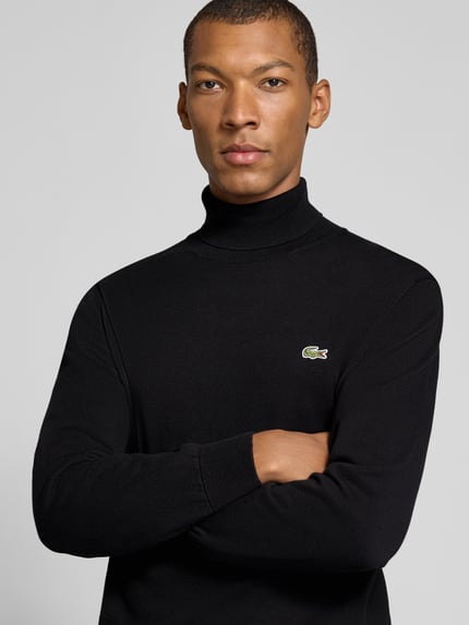 Männermodel trägt schwarzen Regular Fit Pullover aus reiner Baumwolle von Lacoste, feinstrick Textur, Nahaufnahme Oberkörper, Herren Turtleneck-Pullover.