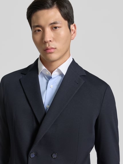 Männermodel trägt Slim Fit Sakko mit Reverskragen Modell 'BERTUE' von CINQUE, Zweireiher, dunkle Farbe, Nahaufnahme Oberkörper. Rückenlänge 73 cm bei Größe 50, Schulterbreite 43 cm, Ärmellänge 62 cm, AufgesetzteTaschen, glatte Struktur.