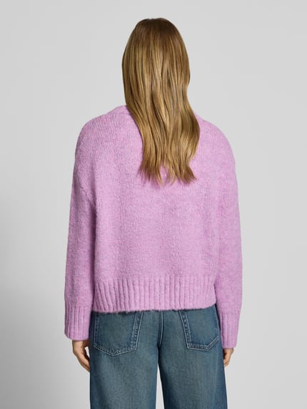 Frauenmodel trägt Pullover mit tiefem V-Ausschnitt von ONLY in Rosa mit grober Strickstruktur, Kombi zu blauer Jeans, Ganzkörperansicht Rückansicht. Damen Pullover von ONLY