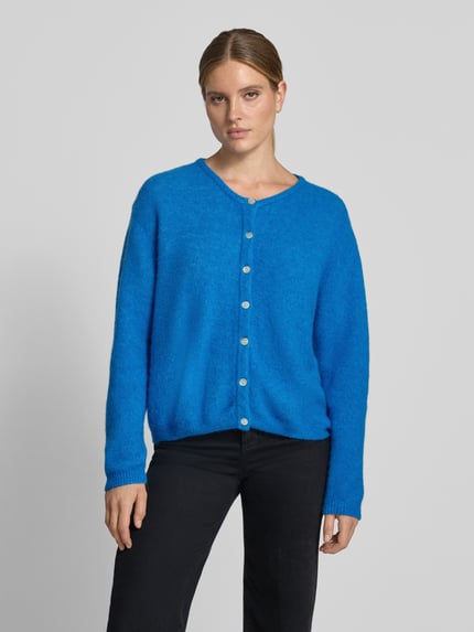 Frauenmodel trägt Relaxed Fit Strickjacke aus Woll-Mix mit Leinen-Anteil von American Vintage in Blau, gerippte Bündchen, Knopfleiste, Langarm, Nahaufnahme Oberkörper.