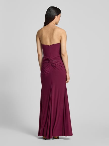 Frauenmodel trägt Slim Fit Abendkleid in Maxilänge mit Gehschlitz von Hey Kyla, Elastischer-Material-Mix, Raffung, Schulterfrei, Rückenlänge 132 cm, Brustweite 28 cm, einfarbiges, glattes Material, Ganzkörperansicht Rückansicht.