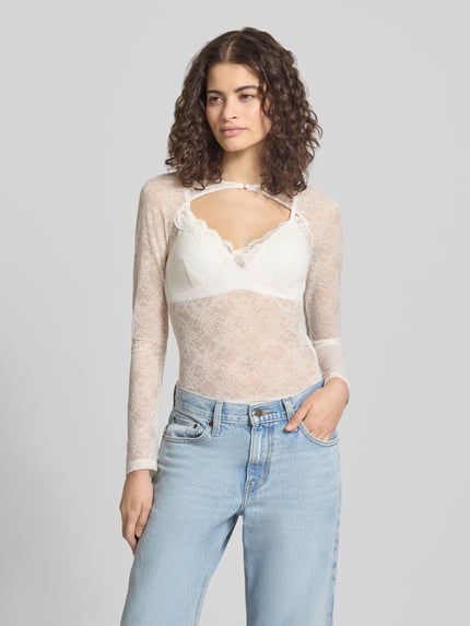 Vrouwenmodel draagt Longsleeve met Cut Out van Gina Tricot in witte semi-transparante kant met materiaalmix met stretch, nauwsluitende pasvorm, knoopsluiting, ruglengte maat S 53 cm, detailopname bovenlichaam.