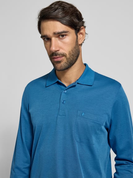 Męski model nosi Regular Fit Poloshirt aus Baumwoll-Mix von RAGMAN w kolorze niebieskim, z kieszenią na piersi, elastycznymi wykończeniami, długi rękaw, Szerokość w rozmiarze M: 70 cm, ujęcie z przodu, zbliżenie na górną część ciała.