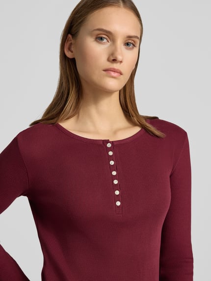 Frauenmodel trägt Slim Fit Langarmshirt aus reiner Baumwolle von REVIEW in Bordeaux mit Rundhalsausschnitt und Knopfleiste, Nahaufnahme Oberkörper.