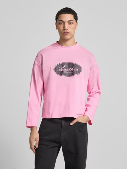 Mężczyznmodel nosi różową bluzkę z długim rękawem Relaxed Fit Longsleeve aus Baumwolle Modell 'Another Vintage' von ANOTHER COTTON LAB z nadrukiem z logo, stójką, bawełna, długość tyłu w rozmiarze M: 63 cm, Ganzkörperansicht von vorne.