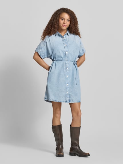Frauenmodel trägt Relaxed Fit Jeanskleid aus reiner Baumwolle von Marc O'Polo Denim in Denim-Optik mit Kurzarm, Mini-Länge, Bindegürtel, Hemdblusenkragen, einreihiger Knopfleiste, Material: reine Baumwolle, Ganzkörperansicht von vorne.