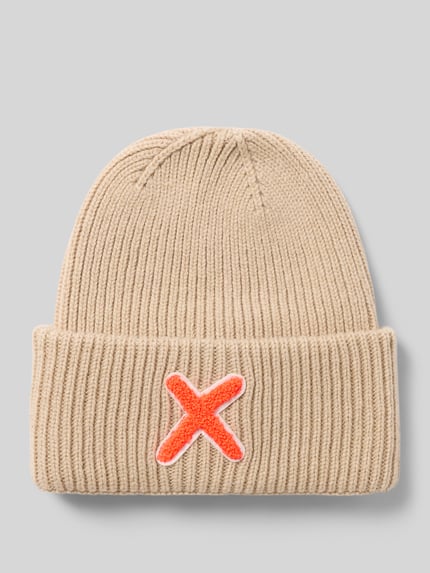 Produktfoto, Mütze aus Schurwolle-Kaschmir-Mix mit Motiv-Stitching von UNIO HAMBURG, grob gestrickt in Beige mit breitem Umschlag und rotem X-Patch.