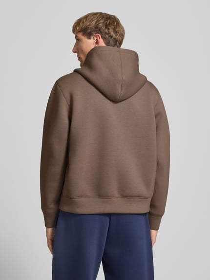 Männermodel trägt Relaxed Fit Sweatjacke mit Zweiwege-Reißverschluss von JACK & JONES in Braun, glatte Textur, Ganzkörperansicht Rückansicht, elastischer Material-Mix, getrennte Känguru-Tasche, elastische Abschlüsse, Rückenlänge und Ärmellänge bei Größe M je 65 cm.