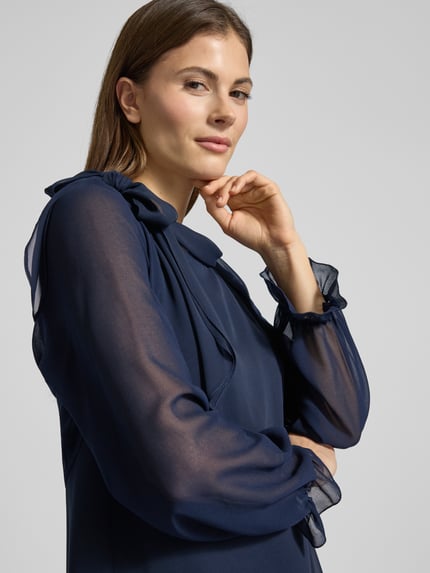 Frauenmodel trägt Relaxed Fit Bolero in semitransparentem Design von V.M., langärmelig mit elastischen Ärmelabschlüssen und Rüschenbesatz, Rückenlänge 41 cm bei Größe 36, Dunkelblau, Nahaufnahme Oberkörper.