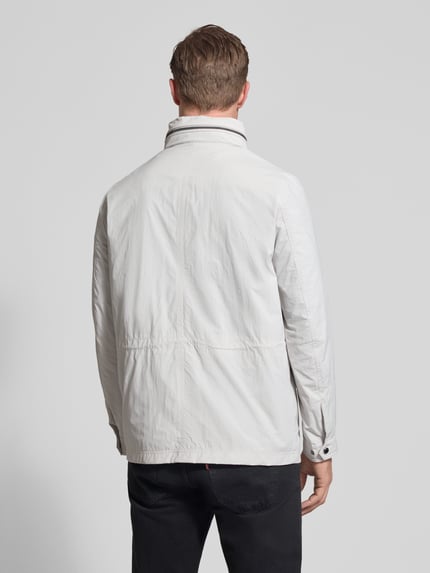 Männermodel trägt Regular Fit Jacke mit opstaande kraag van bugatti in lichtgrijs met borstzakken en logo-applicatie, ganzkörperansicht rückansicht. Ruglengte maat 50: 72 cm, schouderbreedte: 46 cm, borstwijdte: 52 cm, mouwlengte: 68 cm, capuchon opvouwbaar.