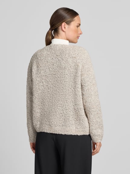 Frauenmodel trägt Relaxed Fit Strickjacke aus Woll-Viskose-Mix Modell 'Sofia' von ZABAIONE in Beige mit grober Textur, Ganzkörperansicht Rückansicht. Damen Strickjacke, durchgängige Knopfleiste, langärmliges Design, V-Ausschnitt, Rückenlänge 62 cm, Ärmellänge 45 cm.