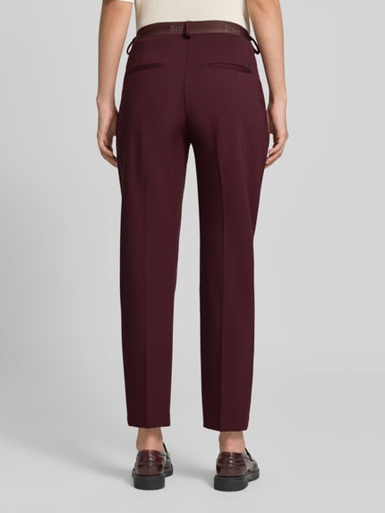 Frauenmodel trägt Regular Fit Chino aus Viskose-Mix Modell 'MARON' von Brax in Dunkelrot, glatte Textur, Damen Schmale Hose, Ganzkörperansicht Rückansicht.