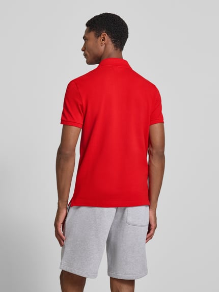 Męski model nosi Slim Fit Poloshirt aus reiner Baumwolle od Lacoste, czerwona koszulka polo, gładka tekstura, widok całej sylwetki z tyłu.
