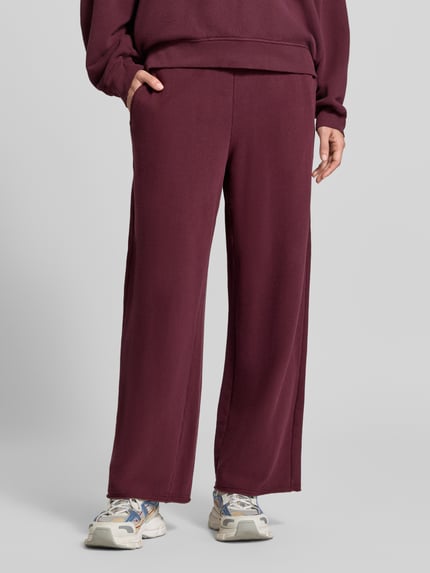 Frauenmodel trägt Straight Fit Sweatpants aus elastischem Baumwoll-Mix von American Vintage in Dunkelrot, Nahaufnahme Unterkörper. Damen Sweatpants, elastisches Material, Modell 'ATUBAY', Bund mit Tunnelzug, Innenbeinlänge 72 cm bei Größe S.