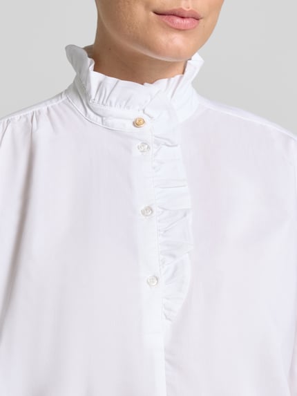 Vrouwenmodel draagt Bluse mit Rüschen und kurzer Knopfleiste van Christian Berg Woman in wit katoenmix met stretch, regular fit, opstaande kraag met ruches, korte knoopsluiting, afgeronde zoom, detailopname bovenlichaam.