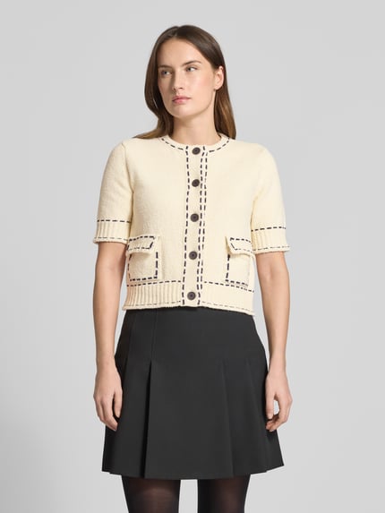 Frauenmodel trägt Slim Fit Strickjacke mit aufgesetzten Taschen von Rich & Royal in Creme mit schwarzen Nähten, Baumwoll-Mix, Nahaufnahme Oberkörper.