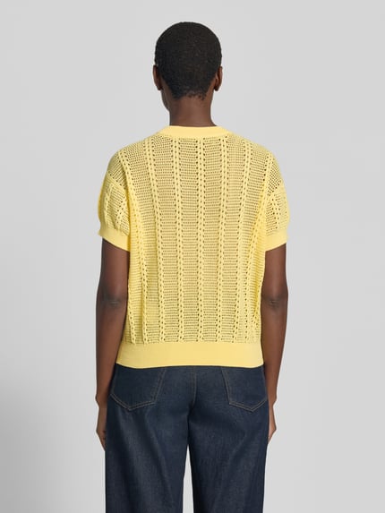 Frauenmodel trägt Relaxed Fit Strick-Shirt aus bawełna-mix Modell 'LUX LIGHT' von Vero Moda, jednokolorowy, ażurowy wzór, okrągły dekolt, krótki rękaw, prążkowane zakończenia, mieszanka bawełny, wykończenie: ażurowa dzianina, Ganzkörperansicht Rückansicht.