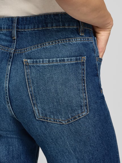 Frauenmodel trägt Wide Fit Jeans aus reiner Baumwolle Modell 'DANILA' von MANGO in mittlerem Blau mit sichtbarer Rückentasche, Nahaufnahme Hüfte, 5-Pocket-Design, Gürtelschlaufen, Knopf- und Reißverschluss.