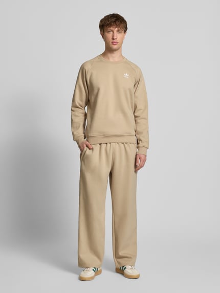 Männermodel trägt Wide Fit Sweatpants mit elastischem Bund von adidas Originals in Beige, Baumwoll-Mix, Logo-Stitching, Ganzkörperansicht von vorne.