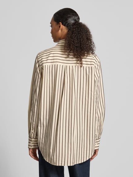 Frauenmodel trägt Loose Fit Langarmbluse aus reiner Baumwolle von ARMEDANGELS, beige mit braunen Streifen, lockerer Schnitt, Ganzkörperansicht Rückansicht.