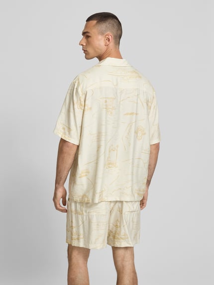 Männermodel trägt Regular Fit vrijetijdsoverhemd uit Viscosemix van MAISON KITSUNÉ, licht beige met grafisch patroon, schouderbreedte 52 cm, mouwlengte 30 cm, ruglengte 71 cm, reverskraag, knoopsluiting, met korte mouwen, Ganzkörperansicht Rückansicht.