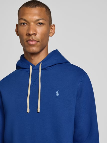 Męski model nosi Regular Fit Hoodie aus Baumwoll-Mix von Polo Ralph Lauren, intensywny niebieski kolor, miękka struktura, zbliżenie na górną część ciała.