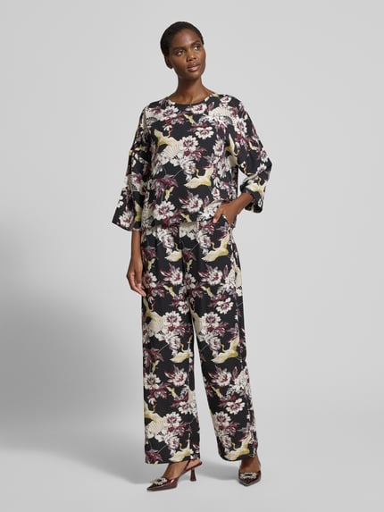 Vrouwenmodel draagt Stoffhose aus Viskose-Mix Modell 'Orelia' van GUIDO MARIA KRETSCHMER WOMAN, wijde pijp, bloemenprint, allover-look, broekzakken, kleuren zwart, crème en roze. Volledige lichaamsweergave van voren.