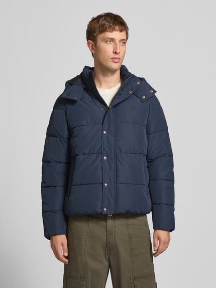 Männermodel trägt Steppjacke mit Kapuze und Reißverschluss von Superdry in Dunkelblau, Regular Fit, Ganzkörperansicht von vorne. Rückenlänge 71 cm, Schulterbreite 50 cm, Brustweite 56 cm, Ärmellänge 83 cm.