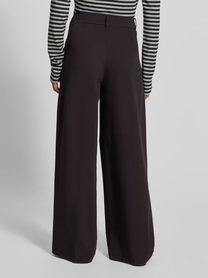 Frauenmodel trägt Wide Fit Hose mit Viskose-Anteil von MYON, dunkel, glatte Oberfläche, Bundfalten, Ganzkörperansicht Rückansicht.