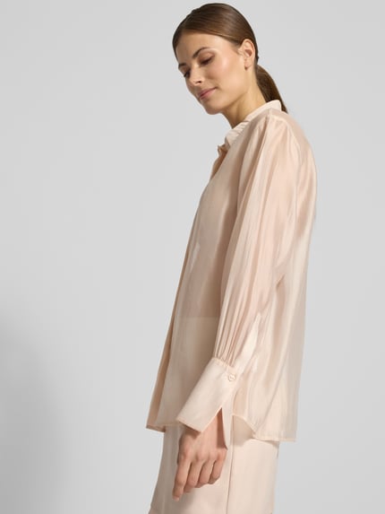 Modelka nosi Organza-Bluse mit großen Manschetten - curated by Vicky Heiler od Damen Hemdbluse SIC curated by vickyheiler, półprzezroczysty materiał, krój regular fit, klasyczny kołnierzyk, długi rękaw z wykończonym mankietem, zapięcie na guziki, kremowy kolor, lekka tekstura, długość tyłu 66 cm, długość rękawa 58 cm, widok całej sylwetki z przodu