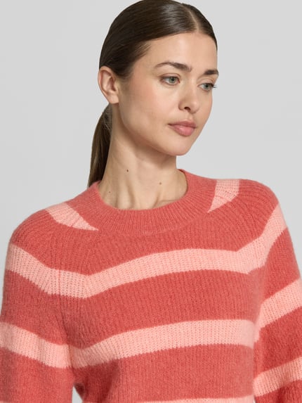 Vrouwenmodel draagt gebreide pullover met 1/2-mouwen van model 'Milania Hope' van MSCH Copenhagen, alpacamix, recht model, ronde hals, ruglengte maat S/M 52 cm, mouwlengte 36 cm, streepjespatroon in roze tinten, zachte textuur, detailopname bovenlichaam.
