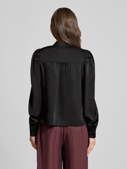 Vrouwenmodel draagt Langarmbluse met Stretch-Anteil Modell 'Rosslyn' van Neo Noir in zwart satijn, losse fit, schouderplooien, ballonmouw, rugaanzicht, context: elastische materiaalmix, V-hals, ruglengte 56 cm, mouwlengte 70 cm.