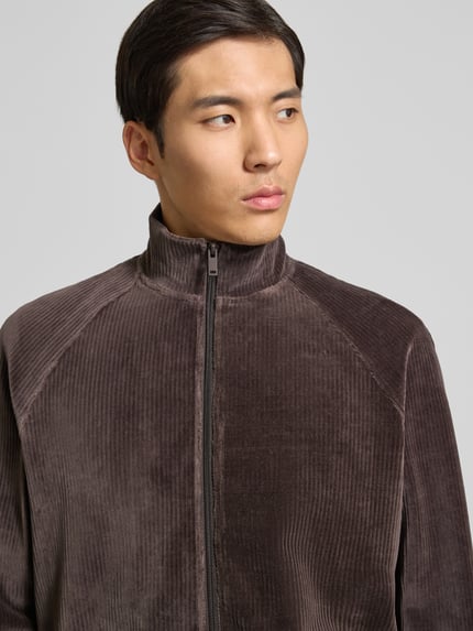 Männermodel trägt Sweatjacke mit Stehkragen von MCNEAL aus braunem Baumwoll-Mix mit Reißverschluss, Nahaufnahme Oberkörper.
