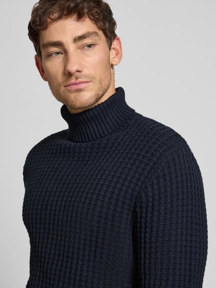Männermodel draagt Regular Fit Rollkragenpullover in Waffel-Struktur Modell 'TOM' van SELECTED HOMME in donkerblauw, gebreid met ribbies op kraag, mouwen en zoom, gemaakt van biologische katoen, Nahaufnahme Oberkörper.