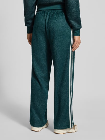 Vrouwenmodel draagt adidas Originals Sweatpants met elastische tailleband, glittereffect, los model, label-stiksel, volledig zicht achteraan.