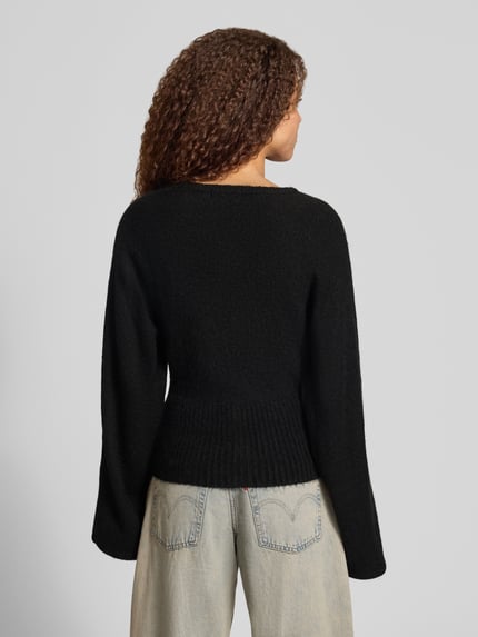 Vrouwenmodel draagt Regular Fit gebreid jack met wol-Anteil van Gina Tricot, zwarte kleur, elastische materiaalmix, ribboorden, lange mouwen, knoopsluiting, ruglengte maat S 53 cm, mouwlengte 49 cm, geheelopname rugaanzicht.