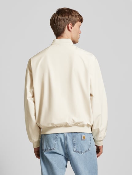 Męskamodel nosi Bomberjacke mit seitlichen Eingrifftaschen Modell 'CHARGE' von Jack & Jones, krój straight fit, kolor kremowy, stehkraag, zamykana na zamek, ściągacze, długość tyłu w rozmiarze M 66 cm, szerokość ramion w rozmiarze M 54 cm, szerokość klatki piersiowej w rozmiarze M 65 cm, długość rękawa w rozmiarze M 64 cm, gładka tekstura, jeansy niebieskie, całkowity widok z tyłu