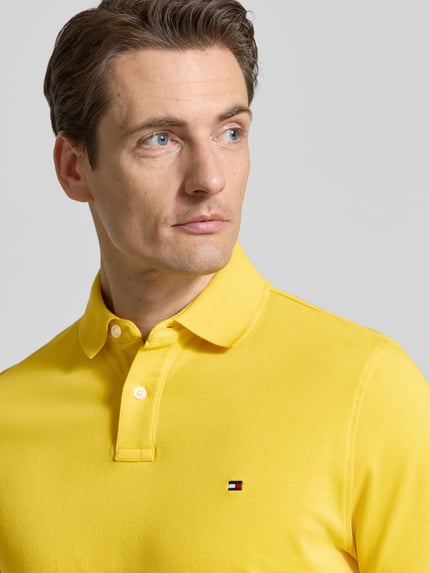 Männermodel trägt Regular Fit Poloshirt aus Baumwoll-Mix von Tommy Hilfiger in Gelb mit Logo-Stitching, Nahaufnahme Oberkörper.