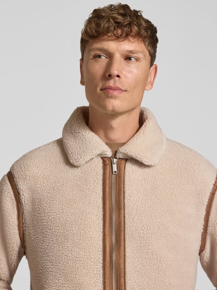 Männermodel trägt Fleecejacke aus Teddyfell von MCNEAL in Beige mit braunen Details, regular fit, omgeslagen kraag, ritssluiting, Nahaufnahme Oberkörper