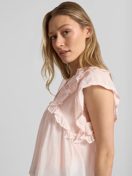 Kobiece modelka nosi bluzkę z bawełny Bluse mit Volants Modell 'Jayla' od Neo Noir, jasnoróżowa, prosty krój, kołnierz z lamówką, falbany, długość tyłu 56 cm w rozmiarze 36, zbliżenie na górną część ciała z przodu