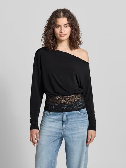 Vrouwenmodel draagt shirt met lange mouwen met asymmetrische hals, kant, nauwsluitend model, model 'Mirelin' van Gina Tricot, materiaalmix met stretch, ruglengte bij maat S 52 cm, voorkant volledige lichaamsopname.