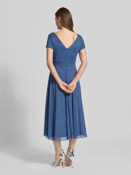 Vrouwenmodel draagt schimmerend cocktailjurk met V-hals van Vera Mont, tule, a-lijn, midi-jurk, ruglengte maat 36 100 cm, borstwijdte 42 cm, glanzende blauwe stof, geheel lichaam van achteren