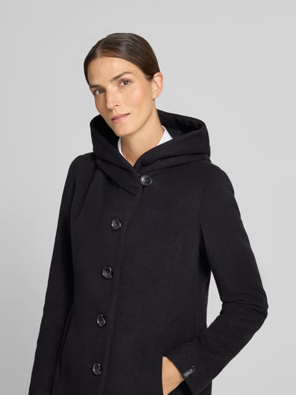 Modelka kobieca nosi czarny Mantel mit Schalkragen und Eingrifftaschen Modell 'Nella' von Milo Coats, krój regular fit, zbliżenie górnej części ciała