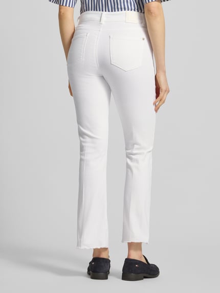 Frauenmodel trägt Bootcut Jeans mit Fransen Modell 'SHAKIRA' von Brax in Weiß mit verkürzter Passform, Ganzkörperansicht Rückansicht.