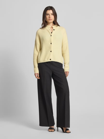 Vrouwenmodel draagt Regular fit cardigan uit alpaca-mix model 'Alpha' van Gestuz in lichtgeel, knoopsluiting, ribdetails, strikstructuur, escorial-wolmix, lengte 55 cm, mouwlengte 48 cm, elastische boorden, frontale full-body aanzicht.