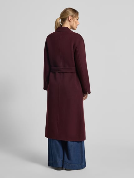 Modelka nosi płaszcz z mieszanki wełny Model 'ALLEGORIA' od OAKWOOD w kolorze bordowym z ozdobnym obszyciem, pasek w talii, widok całej sylwetki z tyłu. Długość tyłu w rozmiarze S: 123 cm, szerokość ramion w rozmiarze S: 46 cm, szerokość w klatce piersiowej w rozmiarze S: 50 cm, długość rękawów w rozmiarze S: 56 cm.