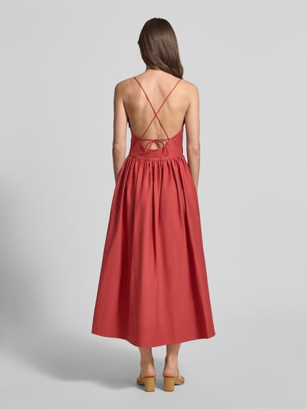 Frauenmodel trägt rotes A-Linien Baumwoll-Midikleid mit Spaghettiträgern und Eingrifftaschen, Modell 'COVER' von SUNCOO PARIS, Ganzkörperansicht Rückansicht.