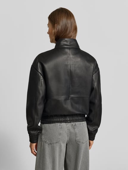 Frauenmodel trägt Lederjacke aus echtem Leder von MYON, lockere Passform, Schwarz, Pattentaschen, gerippte Abschlüsse, Ganzkörperansicht Rückansicht.